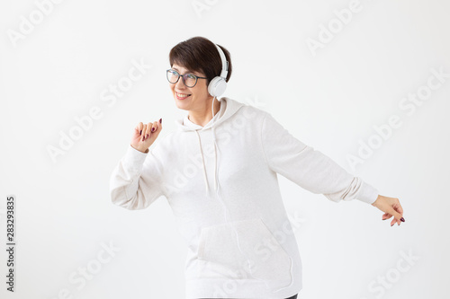 Pretty keen middle-aged woman in glasses and a white sweater listens to her favorite music with headphones on a white background. Online radio and music subscription concept.