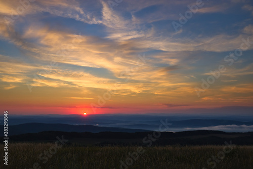 Sun at the moment of rising above the horizon with brightly colored sky slightly cloudy above foggy hills