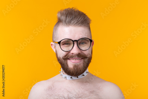 Young positive trendy man hipster with a mustache beard and fetish necklace in shirt posing on a yellow background. Concept of rock and subculture.