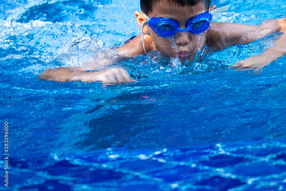 close up asian boy ware a blue glasses diving and swimming in pool and blue refreshing water.