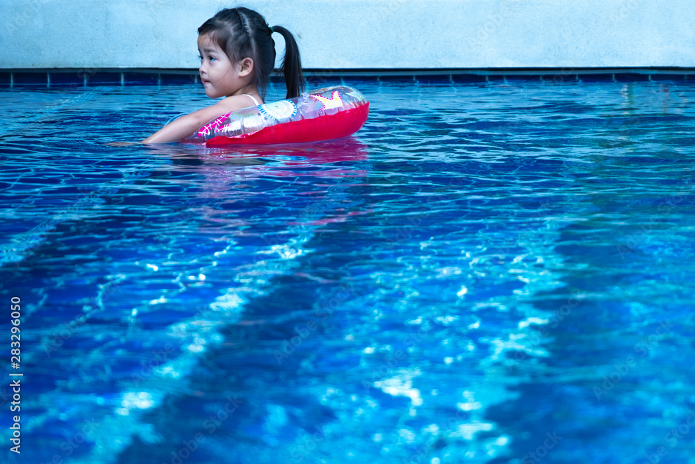 Portrait of cute little asian girl having fun in swimming pool, floating in blue refreshing water with colurful rubber ring