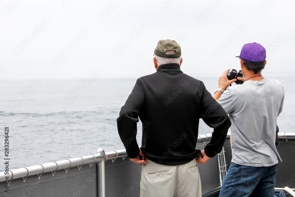 Two men stand at the fence of a boat looking out to the sea