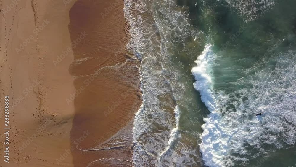 Top down aerial view of wave coming towards the sandy empty beach coastline. Top down aerial view of wave coming towards the sandy empty beach coastline.