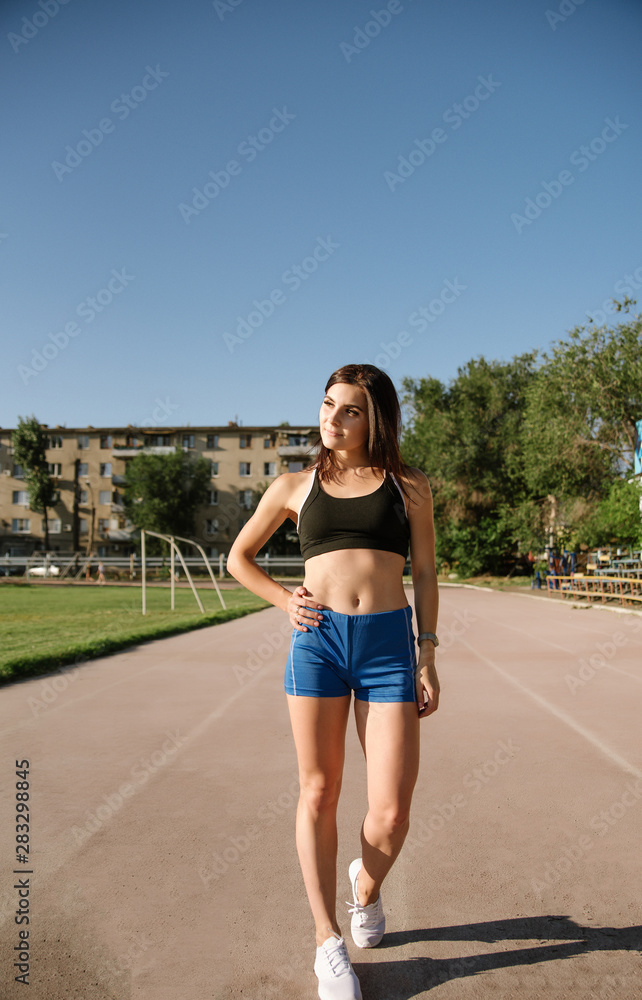 Portrait beautiful woman with a perfect figure in blue shorts and black top posing for the camera on running track at the stadium Portrait beautiful woman with a perfect figure in blue shorts and black top posing for the camera on running track at the stadium