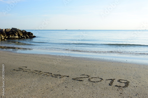 Sommer 2019 in den Sand geschrieben mit dem Hintergrund das Meer und der Sonnenaufgang