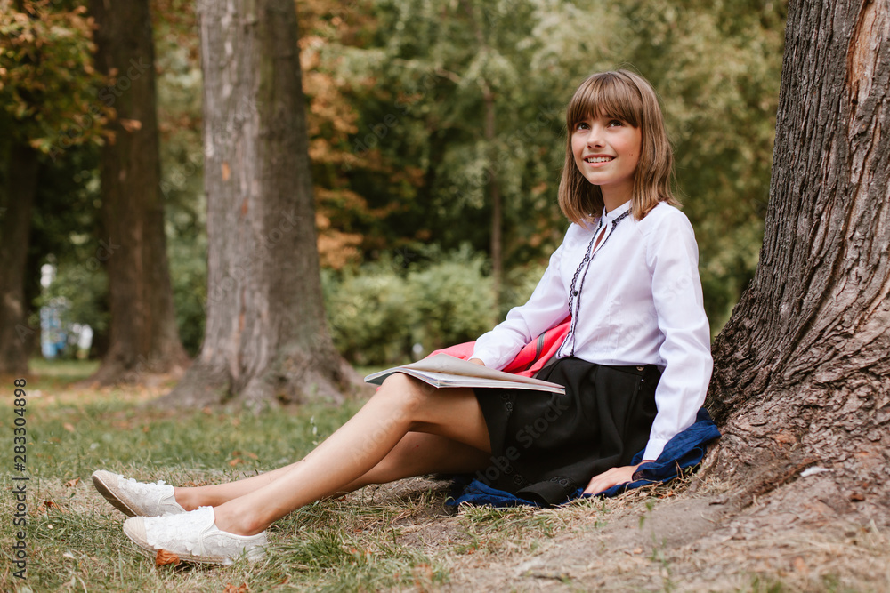schoolgirl sits under a tree in the park