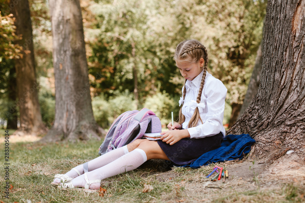 A schoolgirl does lessons in a park under a tree A schoolgirl does lessons in a park under a tree