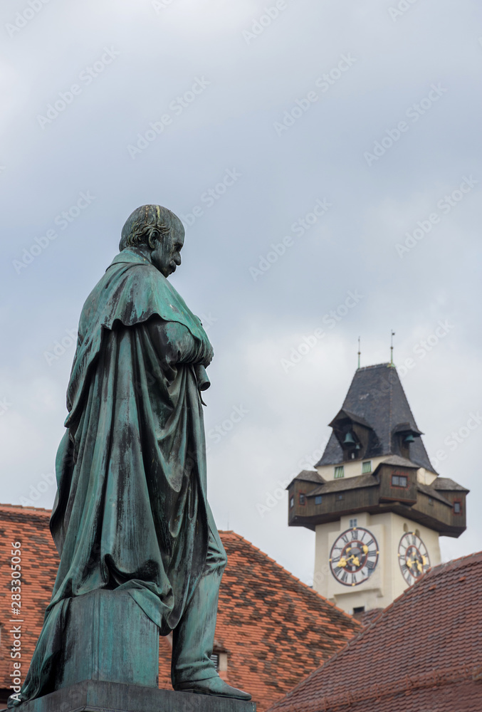 Fototapeta premium Detail of Erzherzog Johann fountain at Hauptplatz (main square) and the famous clock tower (Grazer Uhrturm) in the background, in Graz, Styria region, Austria.
