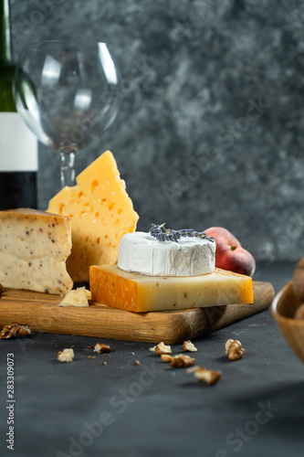 Red wine and cheese. Different types of cheese with nuts, lavander and fig peach on cutting board. Romantic dinner. Copy space for design. Dark background. Soft focus