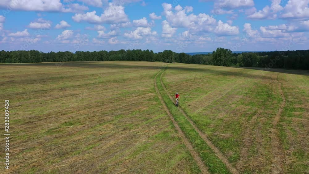 AERIAL view: Boy is riding bicycle on a lone road in field. Beautiful nature with cloudy sky. AERIAL view: Boy is riding bicycle on a lone road in field. Beautiful nature with cloudy sky.