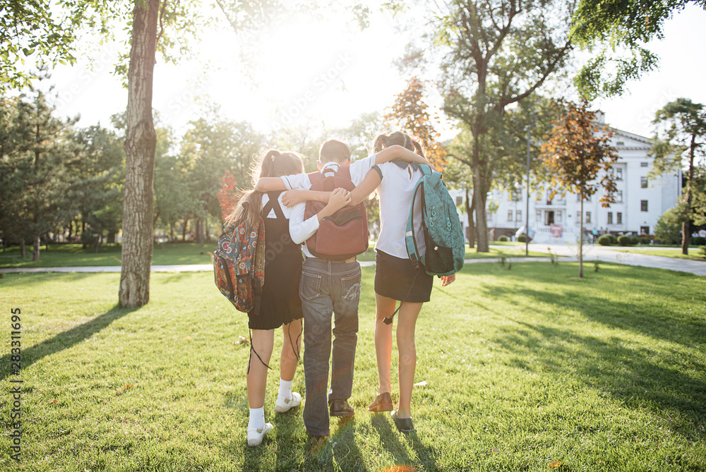 school friends a boy and two girls with school backpacks on their backs walk after class