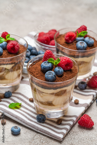Classic tiramisu dessert with blueberries and raspberries in a glass on kitchen towel on concrete background