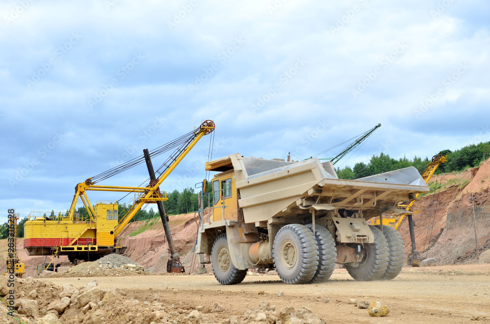 Big mining truck amid huge excavators in an open-pit  dolomite quarry. Loading and transportation of stone ore in a limestone quarry. Excavator and heavy mining dump truck