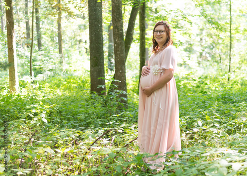 junge hübsche Frau mit Babybauch steht mit einem Kleid im Wald
