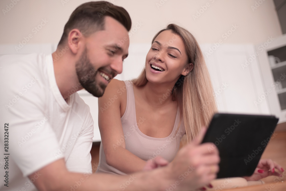 Young couple with digital tablet sitting in kitchen Young couple with digital tablet sitting in kitchen