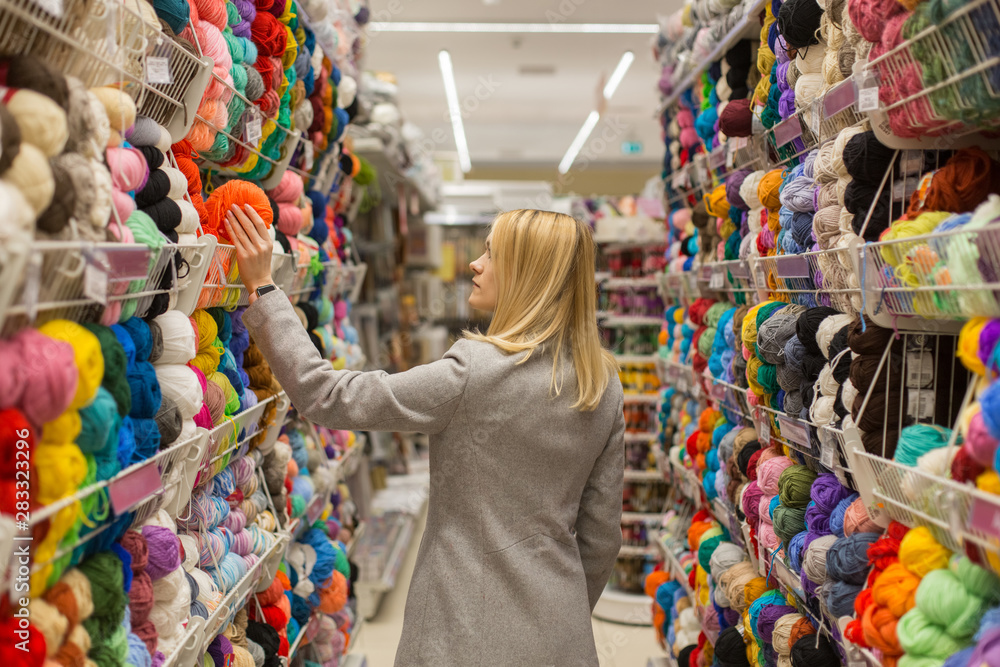 White Woman Choosing Wool Yarn for Knitting in Hobby and Handmade needlework shop.