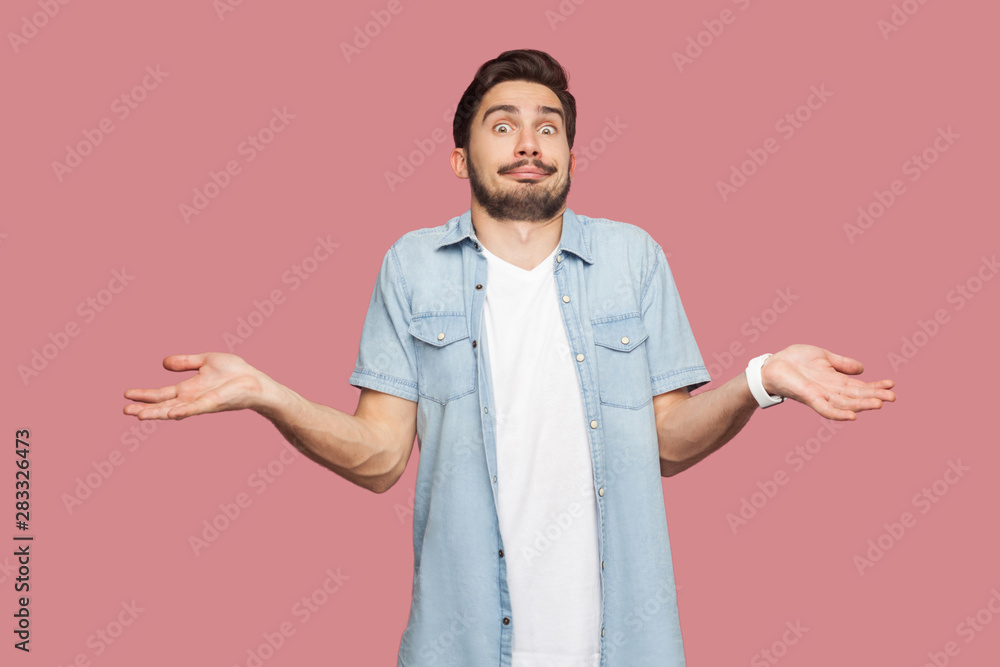 I don't know. Portrait of confused handsome bearded young man in blue casual style shirt standing with raised arms and looking at camera with answer. indoor studio shot, isolated on pink background. I don't know. Portrait of confused handsome bearded young man in blue casual style shirt standing with raised arms and looking at camera with answer. indoor studio shot, isolated on pink background.