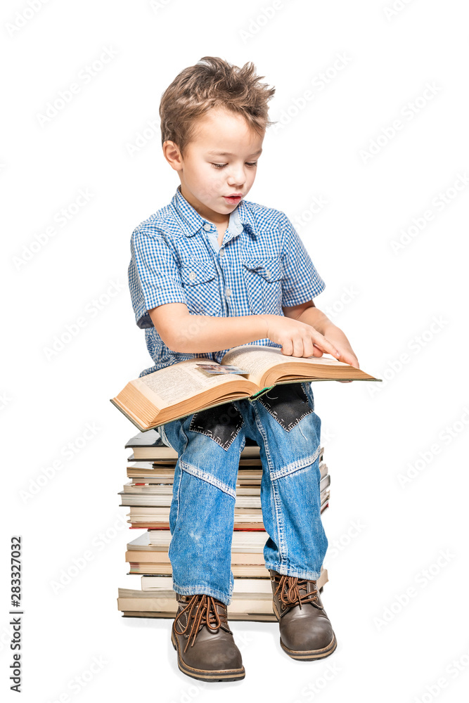Cute boy sitting on a pile of books and reading a book on a white ...