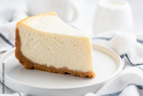 Piece of plain New York Cheesecake on white plate, closeup view. Tasty creamy dessert cake or ice cream cake