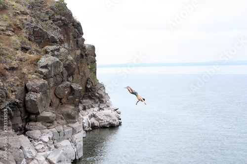 young guy jumps from a cliff into the water photo