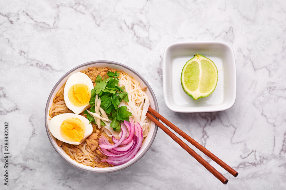 Mohinga at white marble background. Mohinga is a burmese cuisine fish soup with catfish, rice noodles, chicken eggs and lime. Mohinga at white marble background. Mohinga is a burmese cuisine fish soup with catfish, rice noodles, chicken eggs and lime.