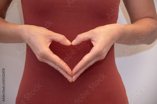 Frau macht ein Herz mit ihrer Hand am Bauch