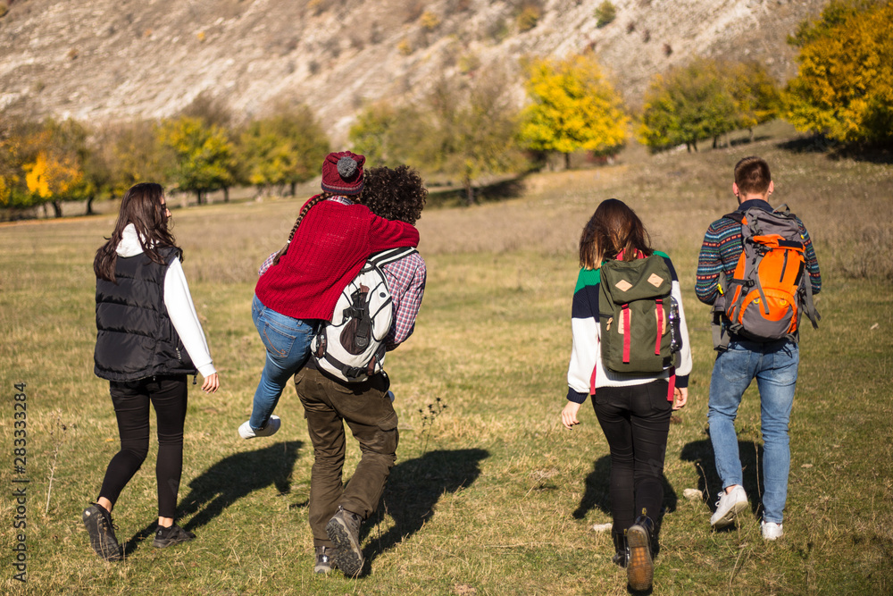 Five friends capturing from the back how going to their exhibition in the mountain, walking tired but with a good mood, they have big trip bags