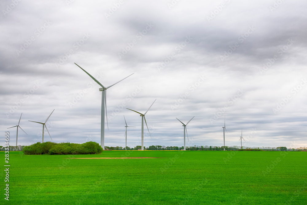 Wind power plant turbines on a green field under sky with clouds. Green energy, renewable sources, save planet Wind power plant turbines on a green field under sky with clouds. Green energy, renewable sources, save planet