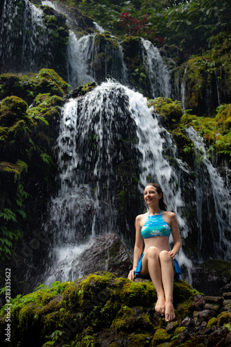 Travel lifestyle. Young traveler woman sitting at waterfall in tropical forest. Banyu Wana Amertha waterfall Wanagiri, Bali, Indonesia.