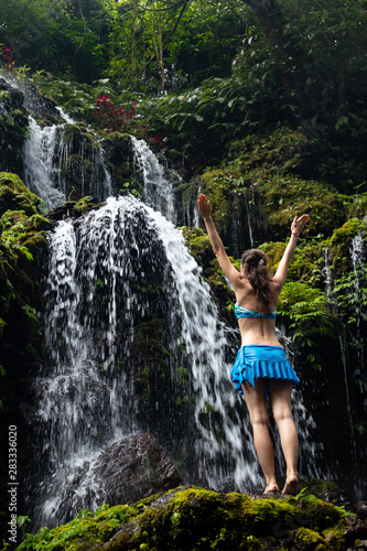 Excited Caucasian woman raising arms in front of waterfall. View from back. Banyu Wana Amertha waterfall Wanagiri  Bali  Indonesia.