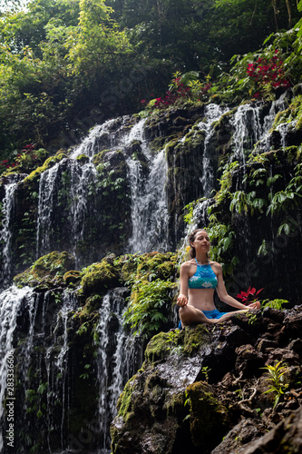 Young Caucasian woman meditating, practicing yoga at waterfall. Banyu Wana Amertha waterfall Wanagiri, Bali, Indonesia.