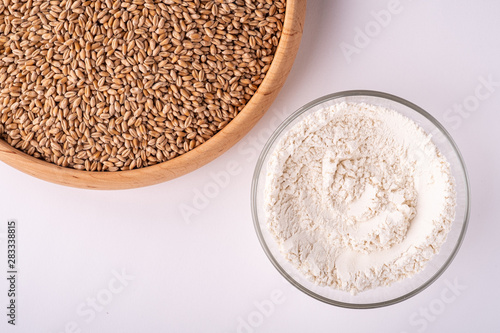 Wheat seeds grains in wooden bowl near with wheat flour in glass bowl, top view, flat lay, isolated on white background, copy space