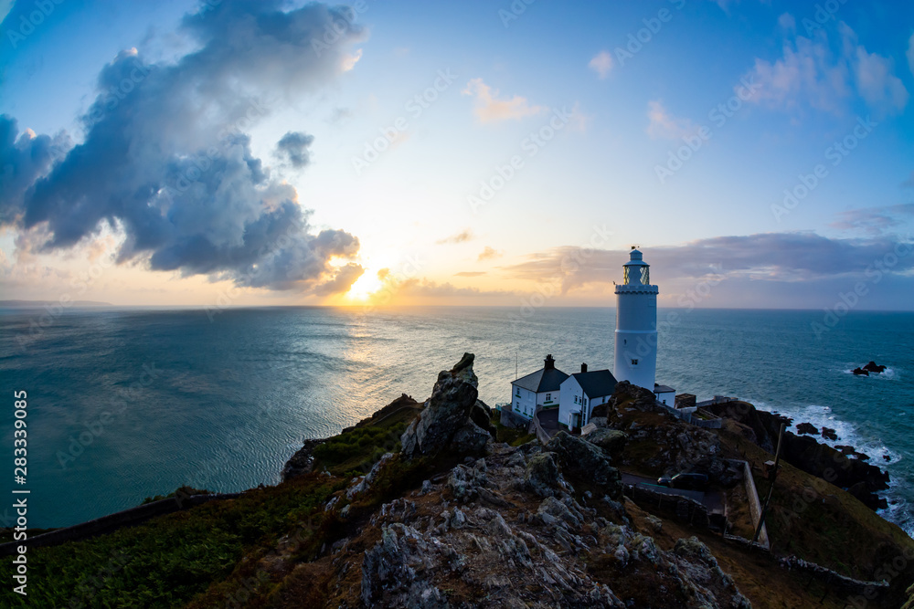Wide angle landscape of lighthouse during sunrise in south Devon in a view from top of a rocky hill