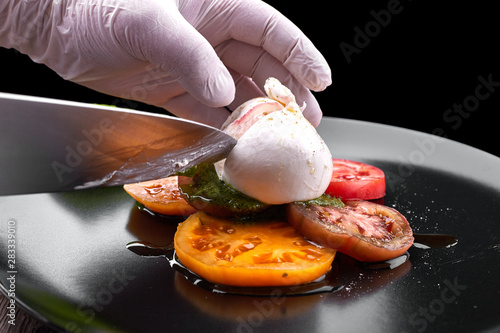 Buratta mozzarella with pesto sauce and tomatoes on a black plate photo