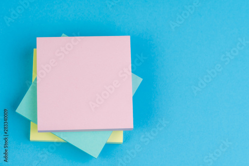 Stack of sticky notes on solid blue background with yellow, blue and pink on top with copy space for writing message using as memo, reminder or business idea and important quote