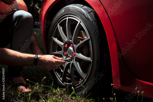 man hand with wrench tightens a beautiful car wheel towards a red car