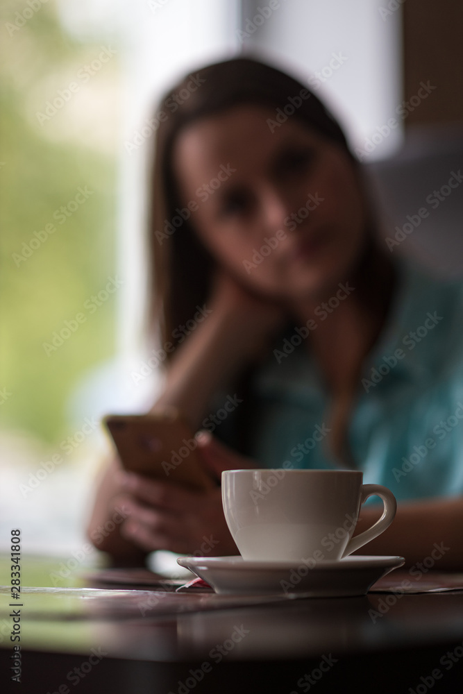A cup of coffee on a table in a cafe in the background a girl. The girl is out of focus. A cup of coffee on a table in a cafe in the background a girl. The girl is out of focus.