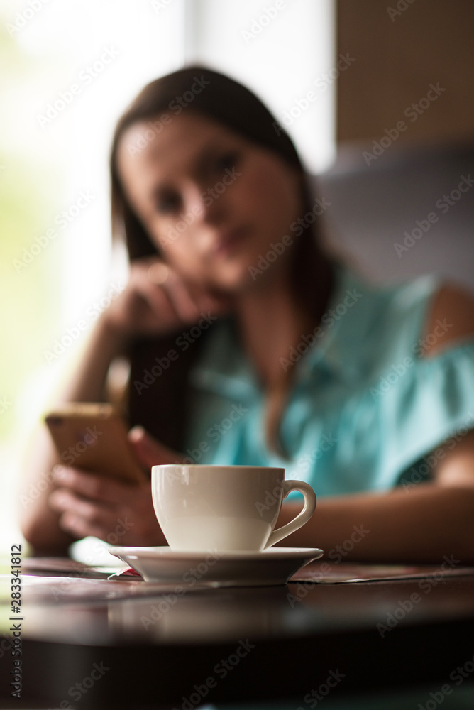 A cup of coffee on a table in a cafe in the background a girl. The girl is out of focus. A cup of coffee on a table in a cafe in the background a girl. The girl is out of focus.