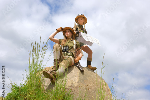 Two young girls dress up as explorers.They pose in  a rocky outdoor area dressed with jungle hats and khaki safari clothes.