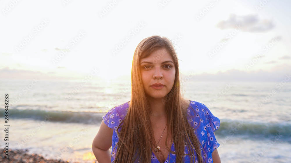Portrait of attractive blonde girl with long hair posing on pebble beach on sunset background. Сoncept beach, sea, pebbles, sand, happiness. Portrait of attractive blonde girl with long hair posing on pebble beach on sunset background. Сoncept beach, sea, pebbles, sand, happiness.