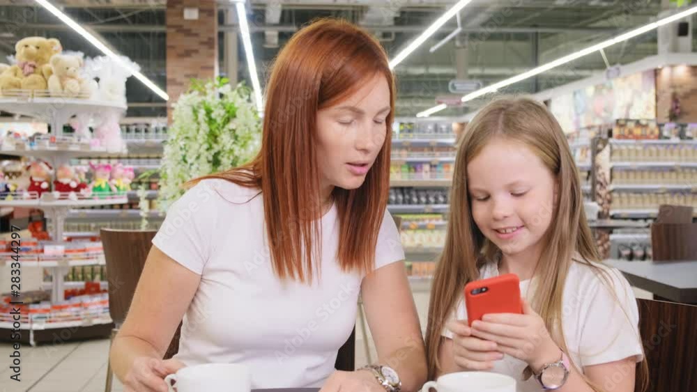 girl and woman mother sitting in restaurant, touching and watching smartphone together girl and woman mother sitting in restaurant, touching and watching smartphone together