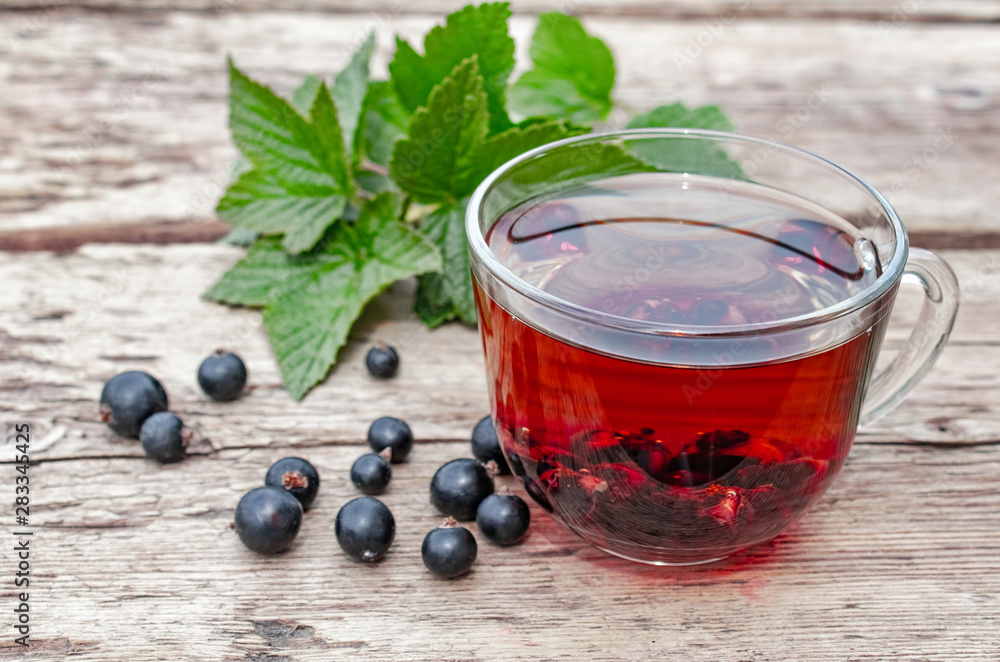 A cup of tea with black currants on a wooden table next to green leaves and currant berries. A cup of tea with black currants on a wooden table next to green leaves and currant berries.