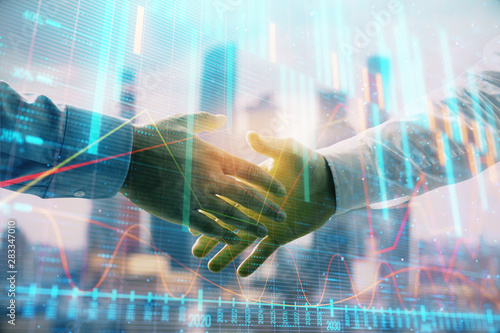 Double exposure of financial graph on cityscape background with two businessman handshake. Concept of stock market deal