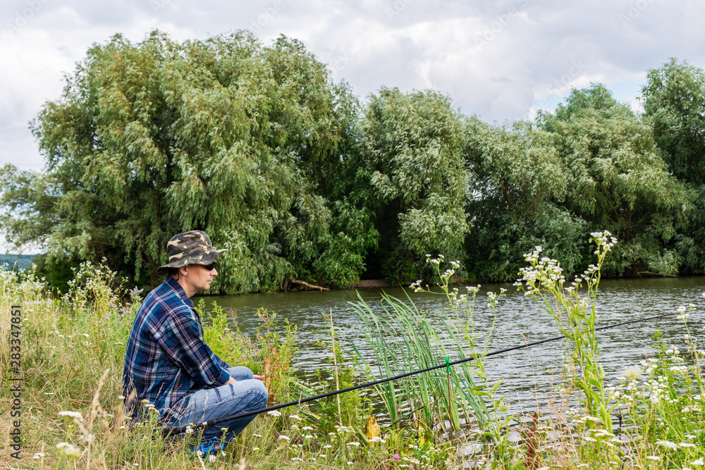 Fisherman fishes on the lake, fisherman man near the water with a fishing rod on a quiet calm evening Fisherman fishes on the lake, fisherman man near the water with a fishing rod on a quiet calm evening