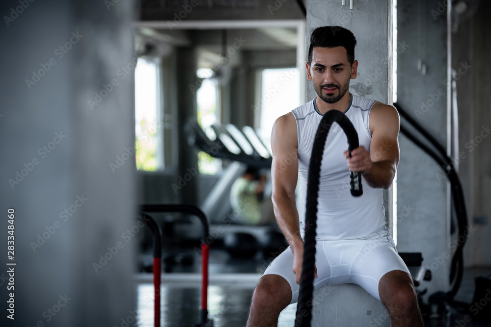 Young adult caucasian athlete sport bodybuilding man in sportswear doing cardio battle rope exercise workout fitness pumping up muscles during training class in gym sport club for strong healthy.