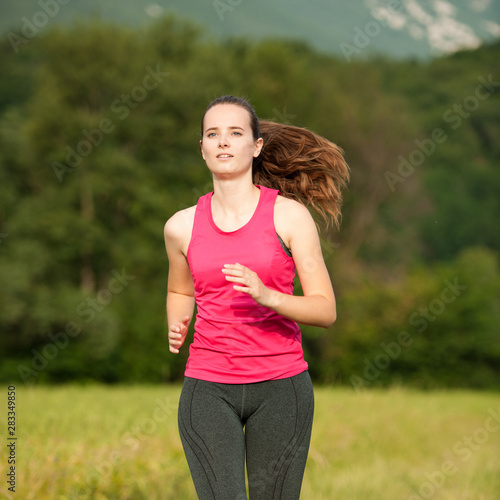 Beautiful young woman workout outdoor runs across meadow in early summer