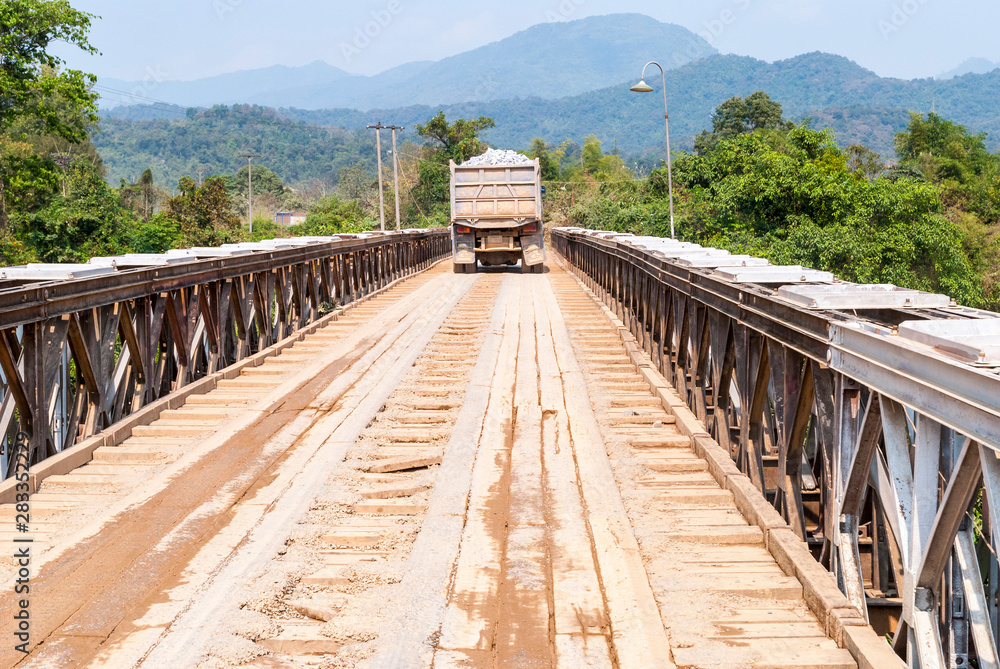 Fototapeta premium Truck driving over wooden bridge, Laos