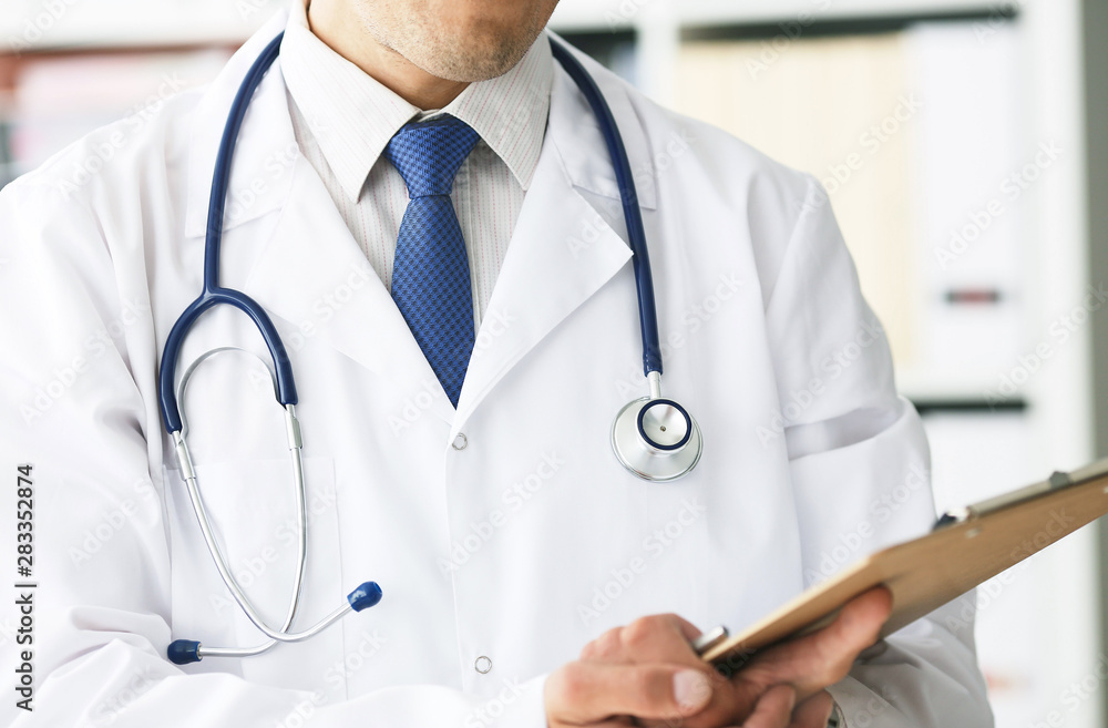 Close-up of clipboard with blank paper in medical doctor hand. Male doctor listens to the patient holding a clipboard with documents for hospitalization. Close-up of clipboard with blank paper in medical doctor hand. Male doctor listens to the patient holding a clipboard with documents for hospitalization.