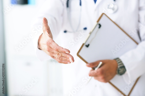 Male medicine doctor hold pad and give arm to shake in office closeup. Friend welcome introduction or thanks gesture. Work examine patient congratulation help exam teamwork deal concept.