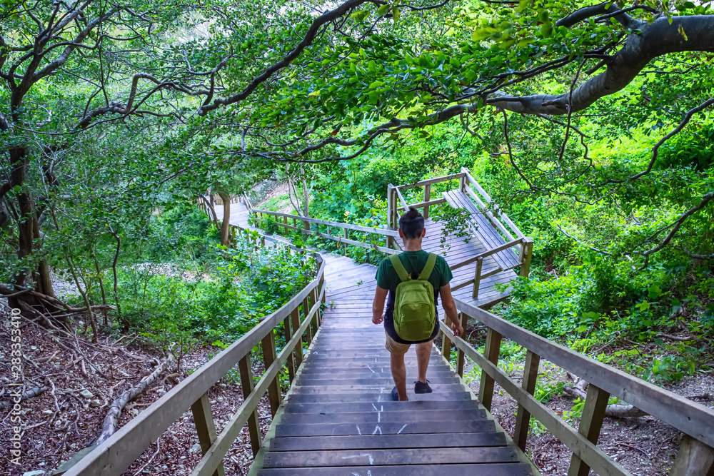 Guy with a backpack goes down a wooden staircase in a mountain forest. Travels. Tourism.